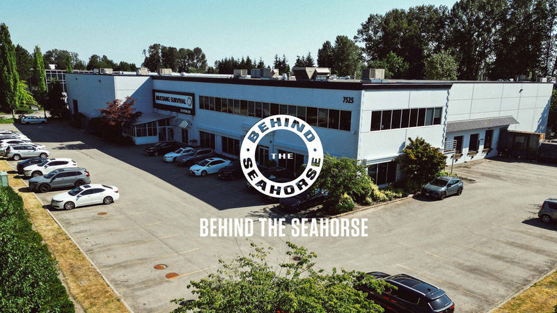 Aerial view of the Mustang Survival headquarters building and parking lot with text overlay: Behind the Seahorse.