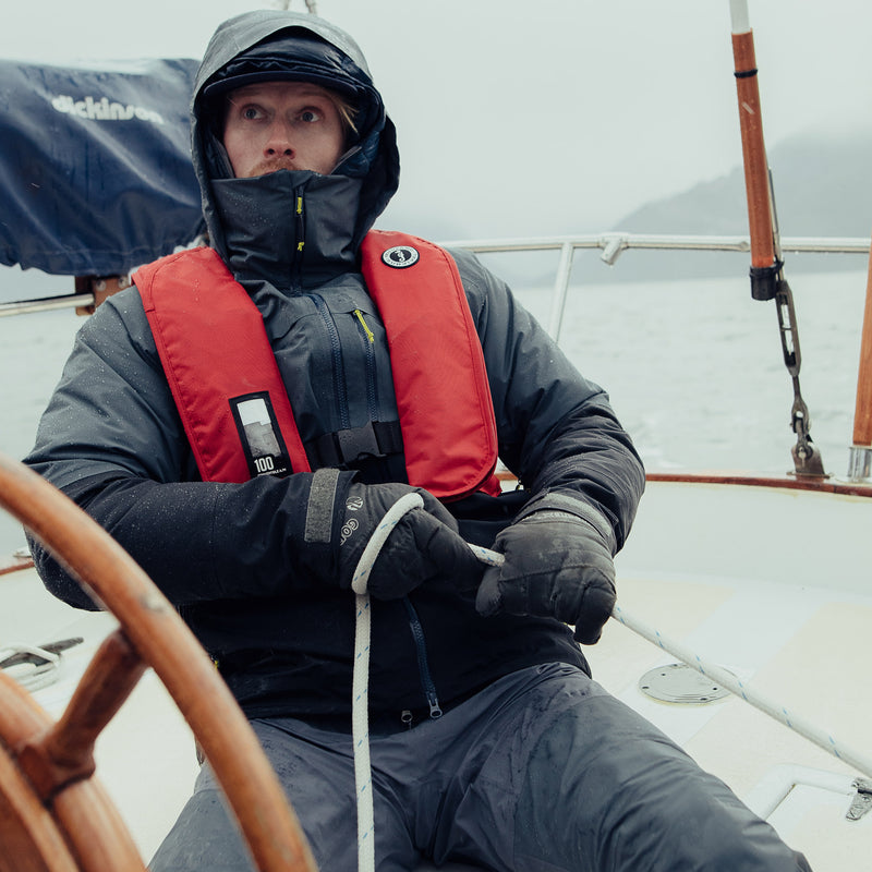 Sailor steering a boat while wearing a red Mustang Survival MIT Inflatable PFD, highlighting functional design and freedom of movement for active boaters.