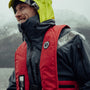 Person wearing a red Mustang Survival MIT Inflatable PFD over a waterproof jacket, demonstrating easy donning and dependable protection in wet conditions.