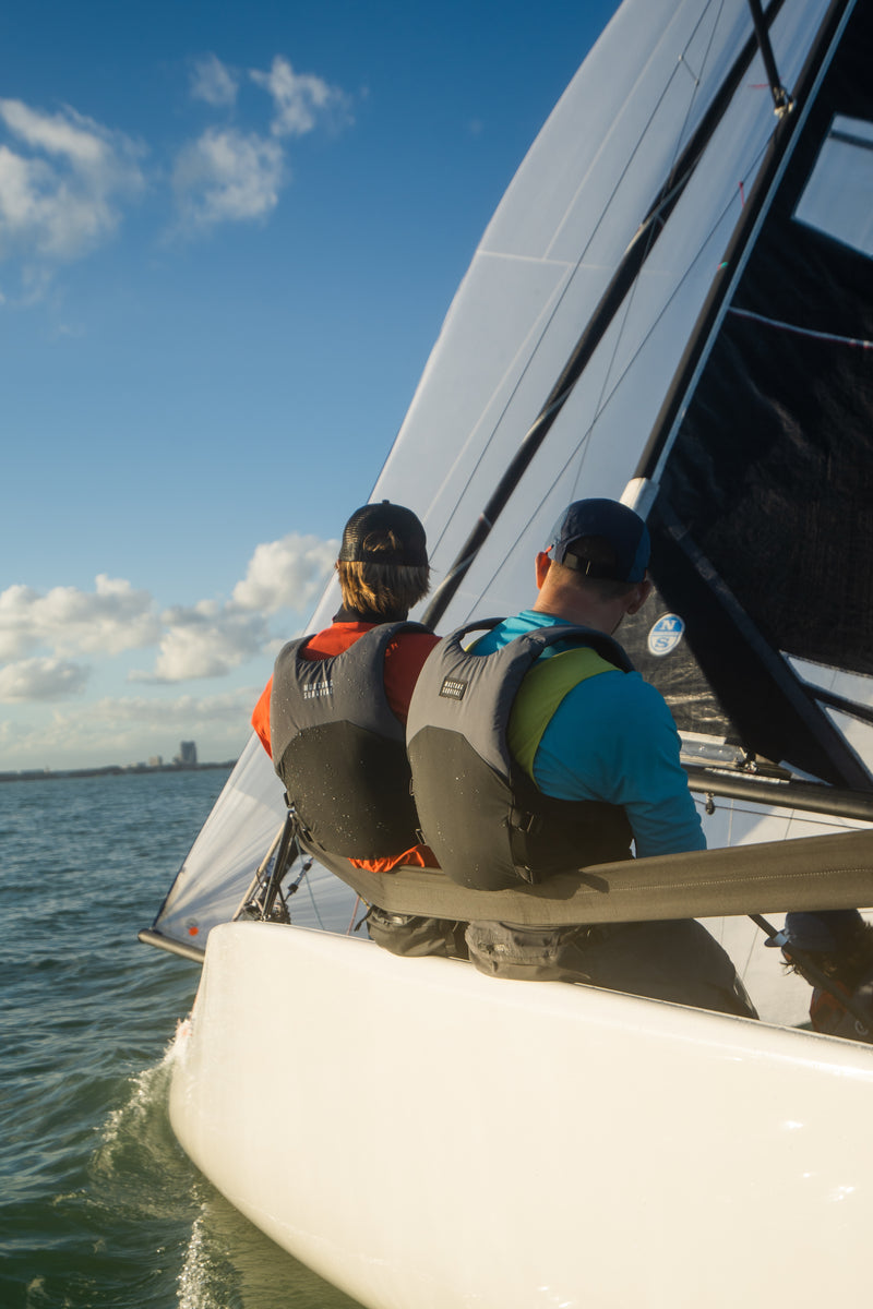 Two people on a sailboat with a clear blue sky and water background