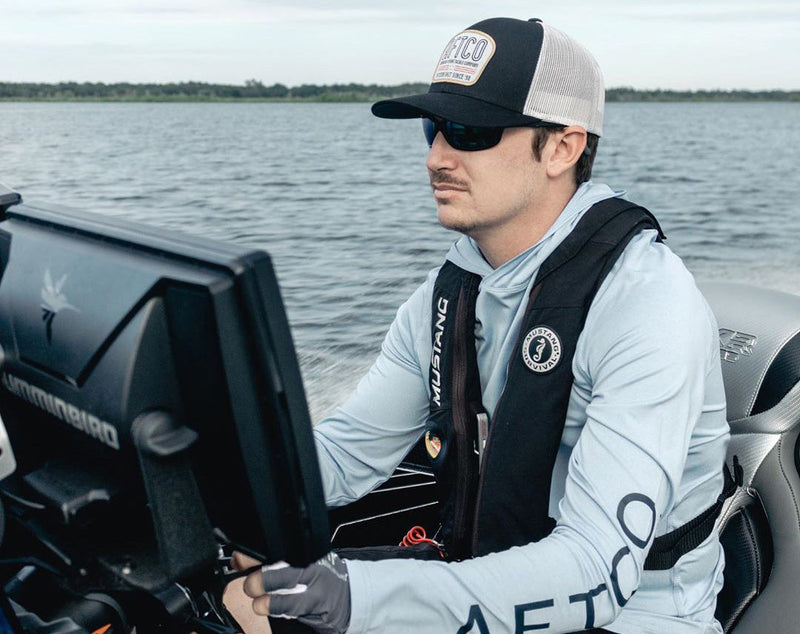Hunter Bland wears an AFTCO cap and a Mustang Survival PFD while looking at a Humminbird fish finder on a bass boat.