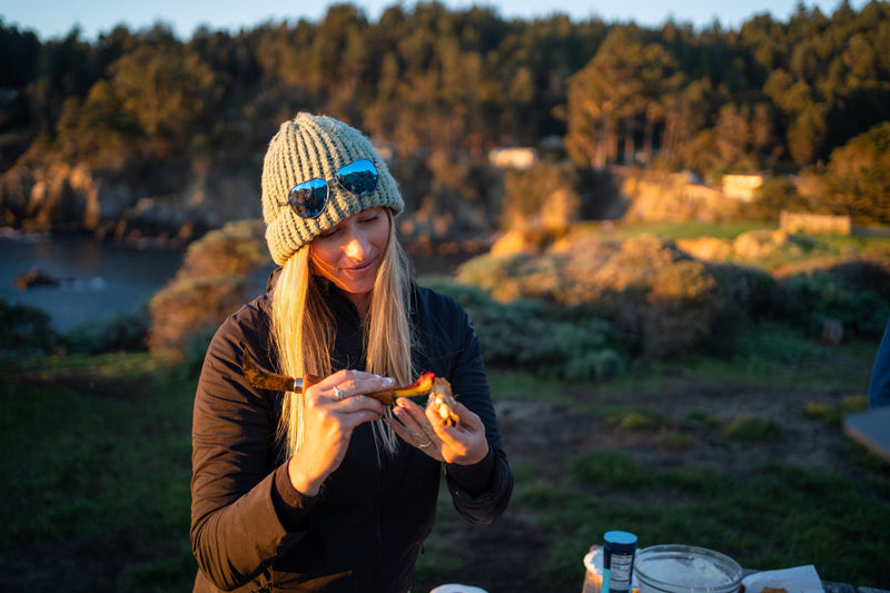Kayak angler Annie Nagel cleans freshly harvested seafood with a small knife while outdoors during golden hour.