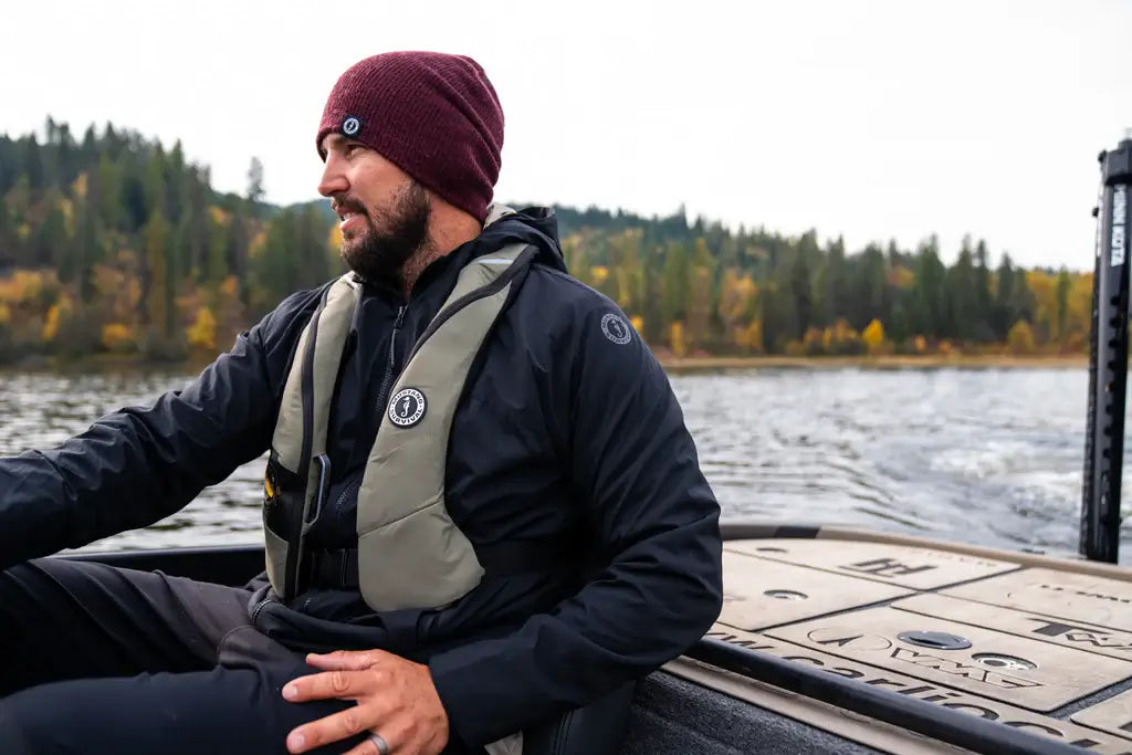 Man wearing a Mustang Survival life jacket, getting a bass into the water during a freshwater bass fishing trip, captured in a half-above, half-below water perspective.