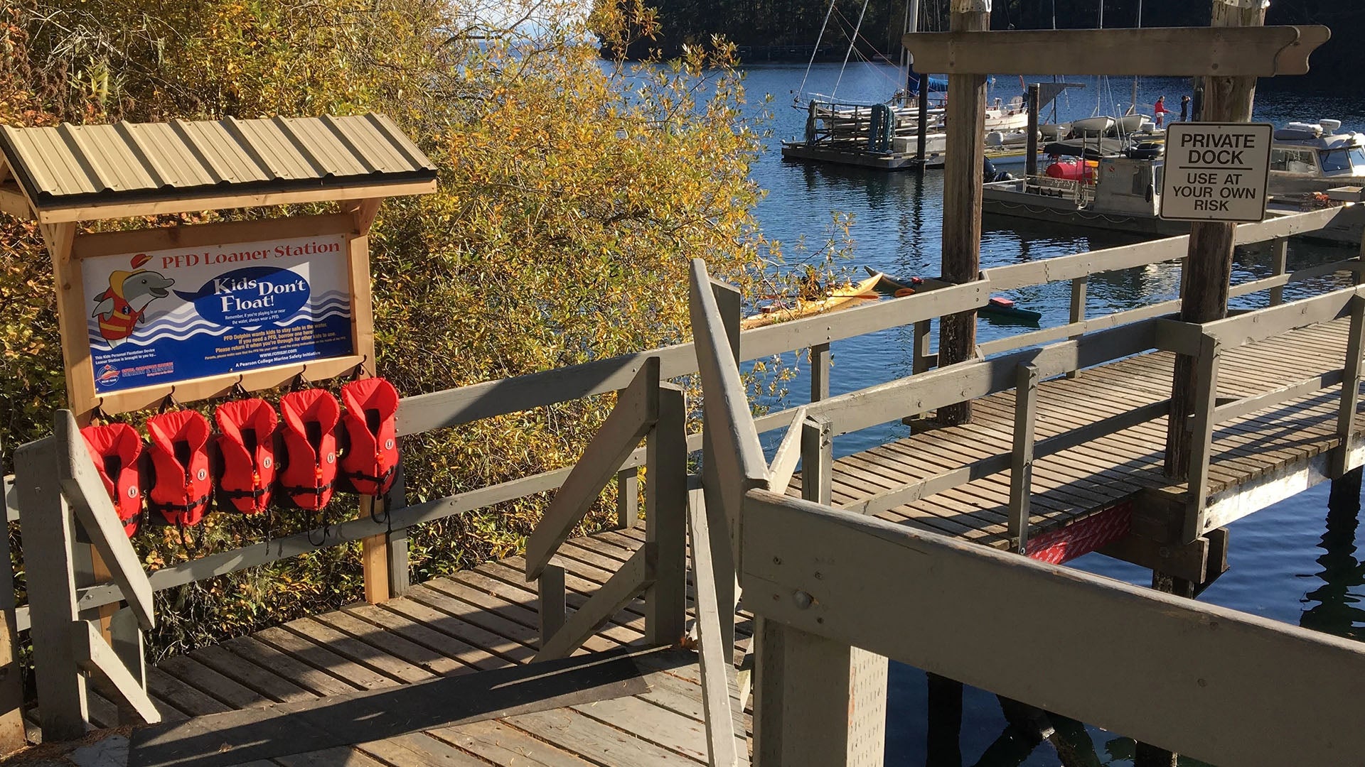 Red life vests on a wooden dock a banner from kids don't float program with a lake and boats in the background. 