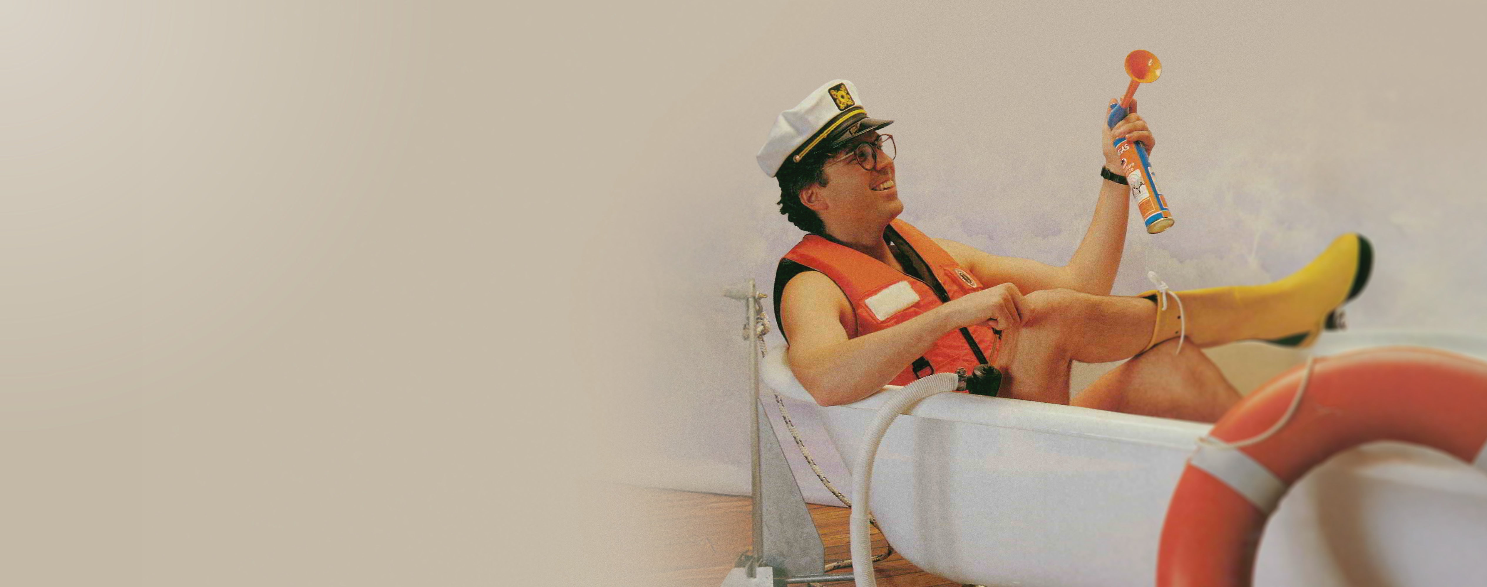 Person in a life jacket and captain's hat sitting on an bath tube with a white background