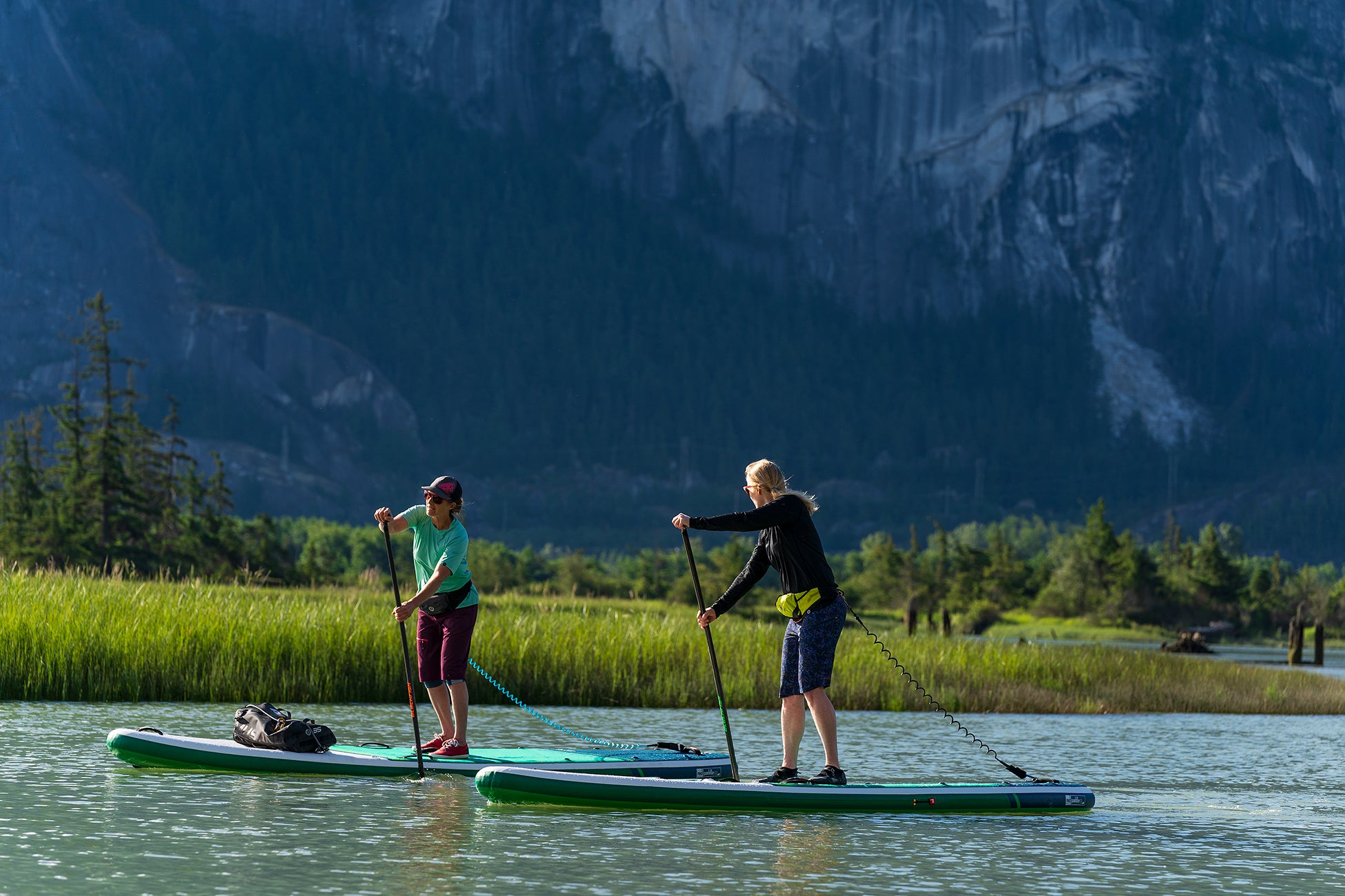 Two people paddleboarding on a lake with mountains in the background